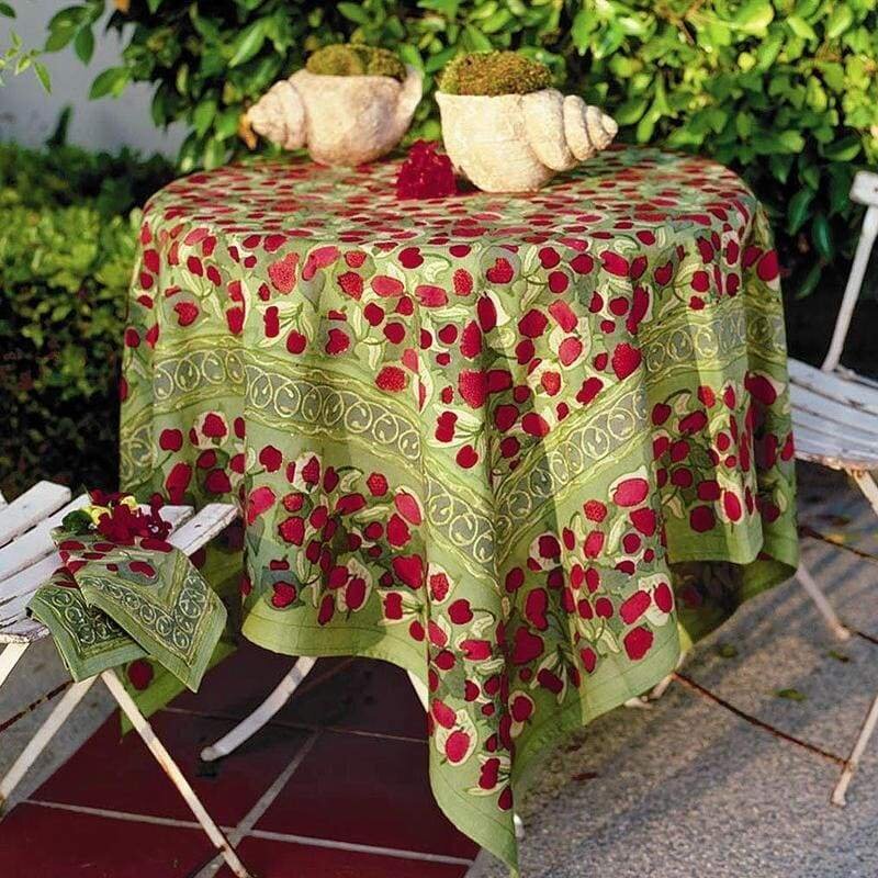Red and green tablecloth featuring a fruit design, draped over a round table with decorative shells and greenery.