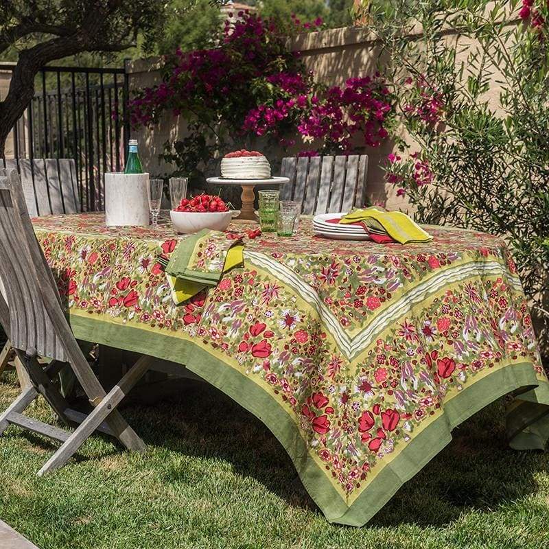 Colorful Couleur Nature Jardin red and green tablecloth draped over a garden table set with food and drinks outdoors.