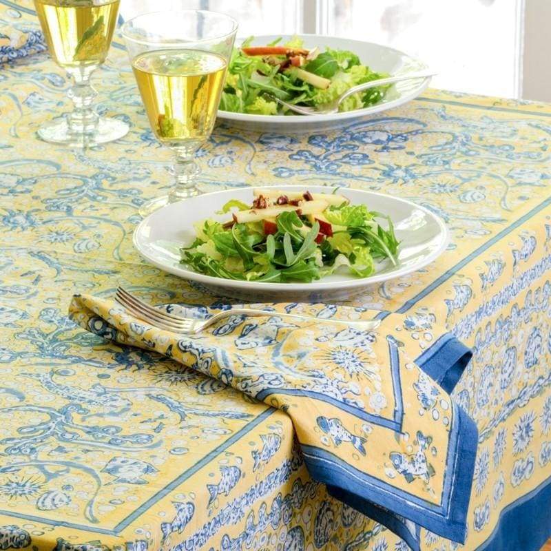 La Mer Blue tablecloth in yellow and blue patterns on a dining table, with plates of salad and glasses of drink.