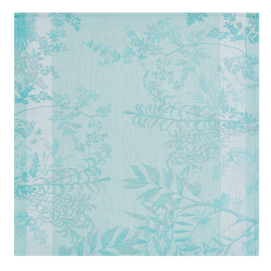 Blue napkin featuring a delicate Jardin d'Eden botanical design with intricate leaf patterns on a textured background.