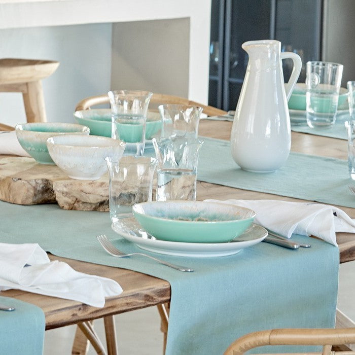 Casafina Taormina cereal bowl displayed on a dining table with a light blue table runner, surrounded by glassware and other dishes.