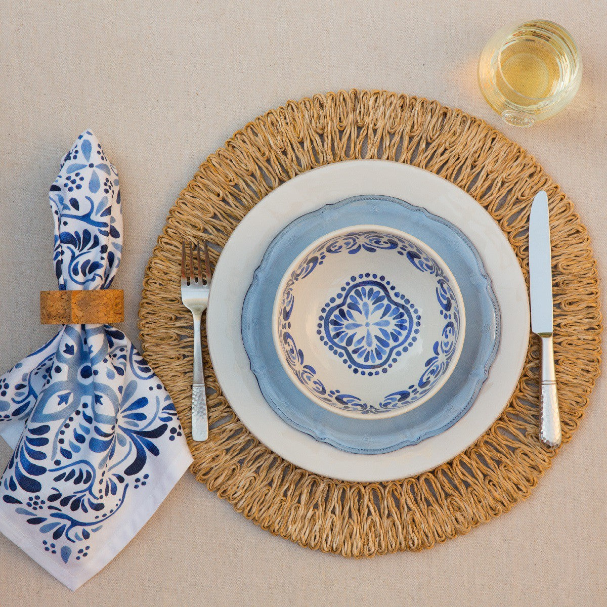 Set of four Juliska Iberian Journey Indigo Napkins displayed elegantly on a woven placemat with a blue and white plate, fork, and knife.