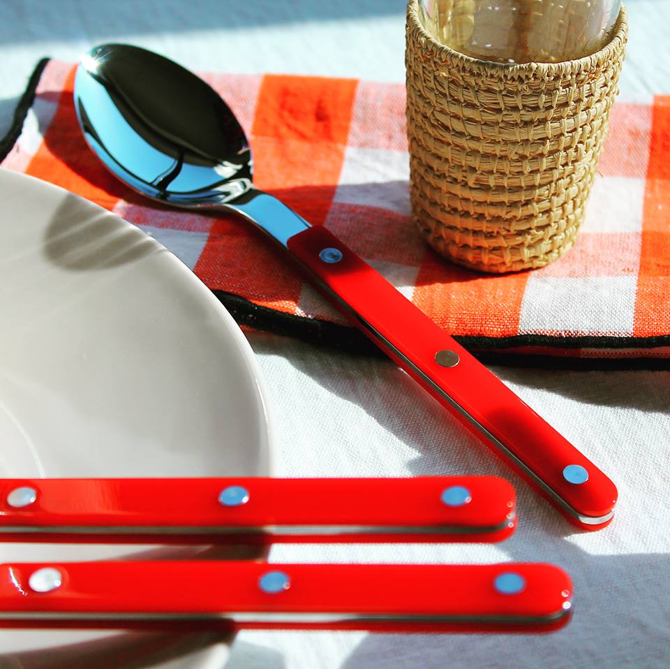 Shiny Sabre Paris Bistrot serving set featuring a spoon with a vibrant red handle, displayed on a checkered napkin.