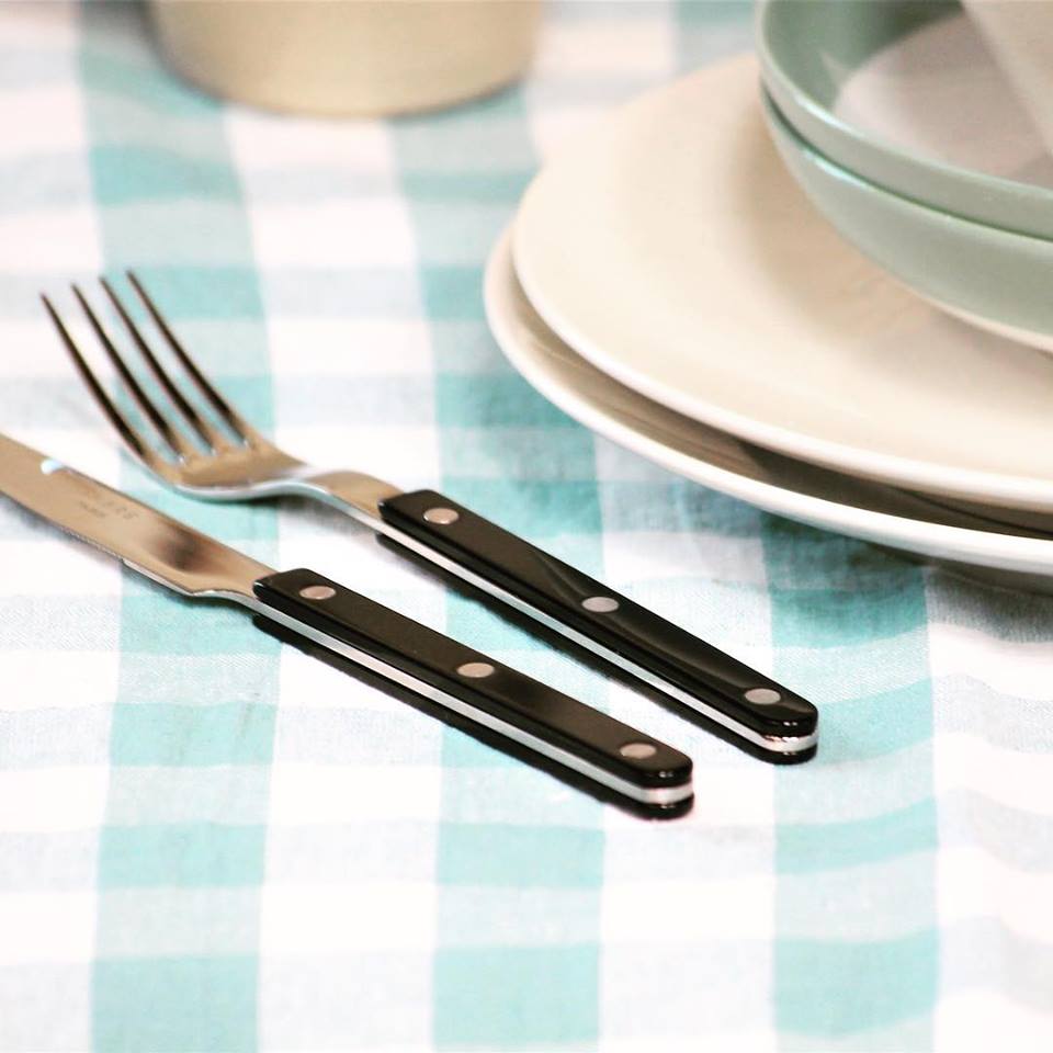 Shiny Sabre Paris Bistrot cheese knife with black handle, placed next to a fork on a checkered tablecloth.
